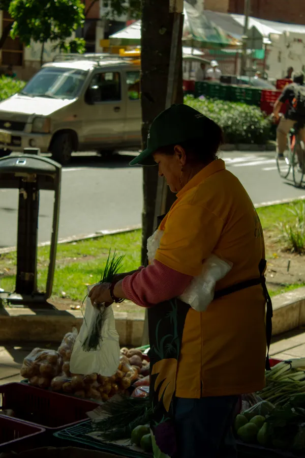 Vendedora de verduras atendiendo su puesto en la acera