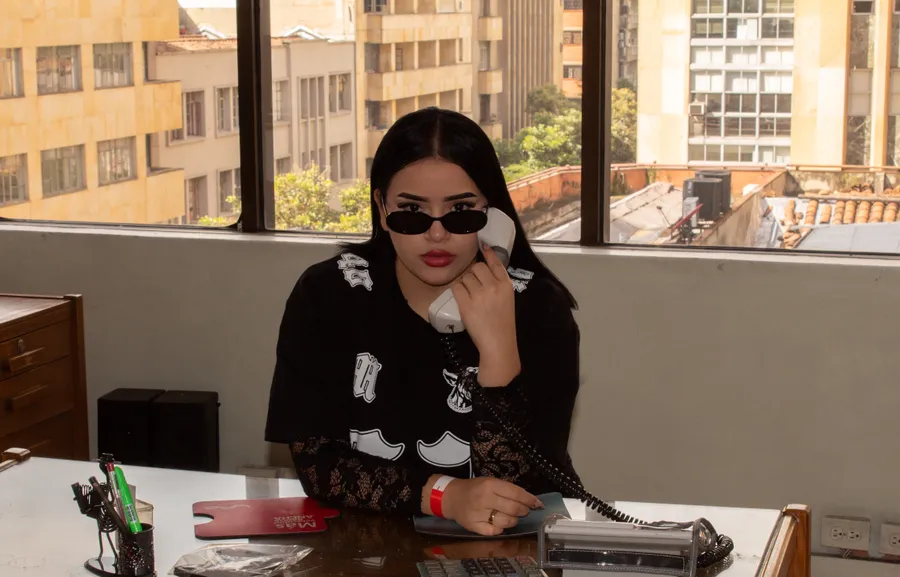 Mujer con gafas de sol junto a una ventana, con la ciudad al fondo