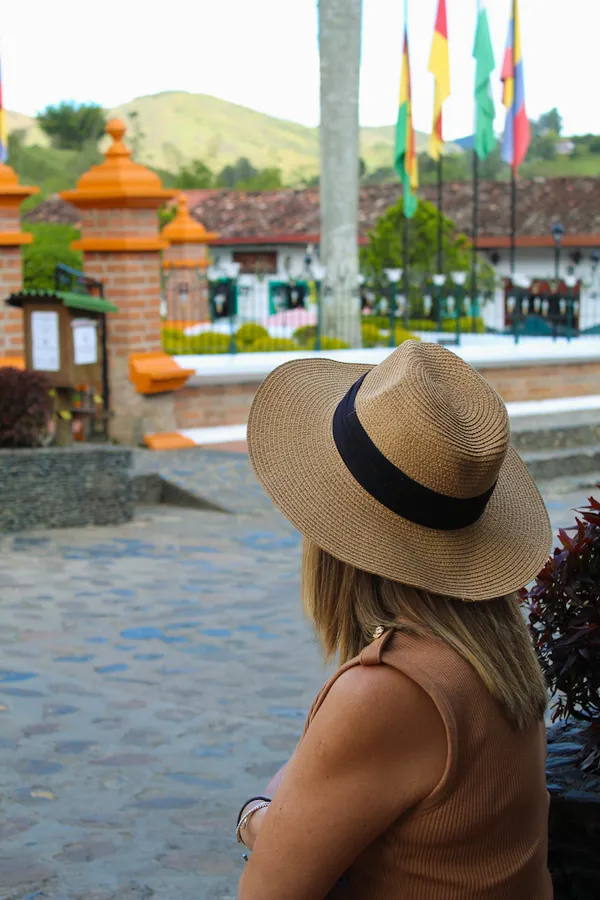 Mujer de espaldas con sombrero, mirando un pueblo embanderado